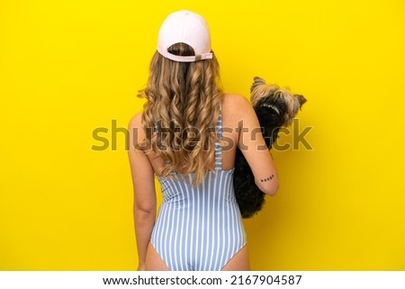 Young woman holding a puppy isolated on yellow background in back position