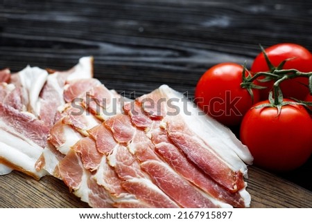 Parma ham slices on dark wooden background with tomato, top view, flat lay