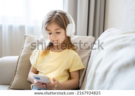 child wear modern headphones relax on couch at home talk speak on video webcam call on cellphone. 