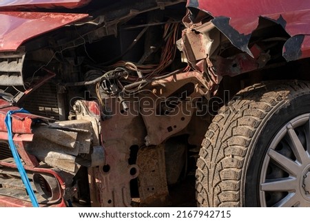 Broken corner of a red car close-up. Damage to the bumper and front fender. Destroyed front headlight. The concept of road accident. Royalty-Free Stock Photo #2167942715