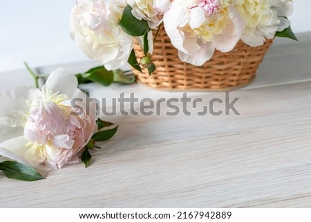 Light peonies in a wicker basket on a white wooden background. Seasonal flowers as a gift for a birthday, wedding decoration or other celebration. Copy Space