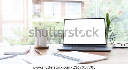 Modern office desk with open laptop computer white screen mockup, financial and marketing report, calculator and supplies.
