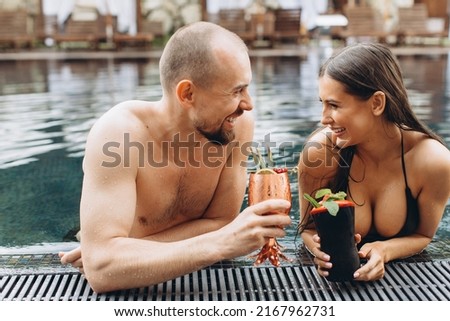 Charming couple relaxing in the pool and enjoying cocktails in summer