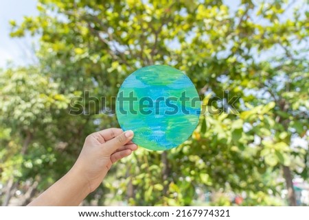 Hand holding earth sign up with natural environment sky and tree as background. Environment protection concept using paper cut planet earth symbol.