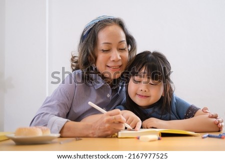 Grandmother with granddaughter drawing picture, enjoying free time on weekend at home together.