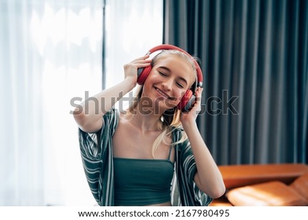 Portrait of happy millennial girl in modern headphones dance listen to music relax in living room.