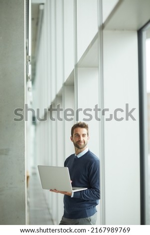 A successful business only needs one great idea. Cropped shot of a handsome young businessman standing indoors alone and using his laptop during the day. Royalty-Free Stock Photo #2167989769