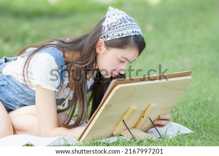 Beautiful teenage girl drawing a picture in the park with easel, palette and paintbrush
