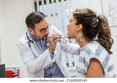 Doctor using inspection spatula to examine patient throat. ENT doctor doing throat exam of a woman. patient opened her mouth to throat check-up Royalty-Free Stock Photo #2168008549