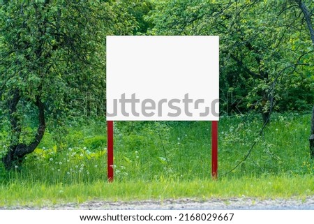 White empty signboard with space for mockup stands on summer garden. Information blank banner on nature background.