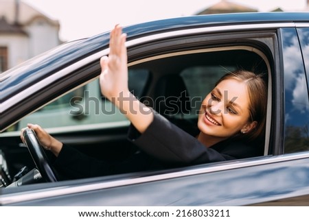 Young smiling woman greeting with hand from car. Cheerful caucasian girl welcome somebody sitting in automobile Royalty-Free Stock Photo #2168033211