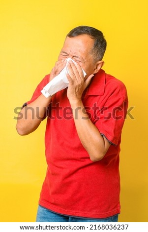 Asian pensioner getting unwell, having influenza and sneezing isolated on yellow background.  Royalty-Free Stock Photo #2168036237