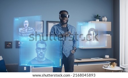 African American man wearing VR goggles at online business meeting in meta universe cyberspace talking with colleagues over video conference, holographic windows in front of him Royalty-Free Stock Photo #2168045893