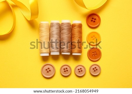 Thread spools, buttons and ribbon on yellow background