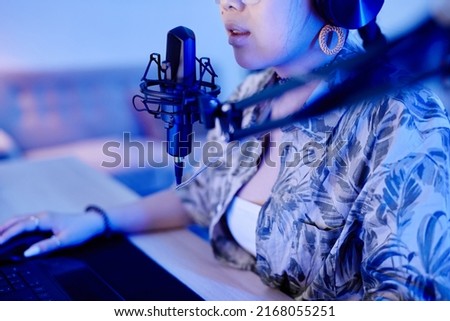 Closeup of young teenage girl playing video game on PC and speaking to microphone while streaming live in blue neon light