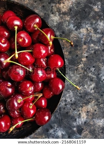 Ripe red cherries on a metal rustic retro plate on a black concrete background with copy space. Flatlay with summer fruits and berries.