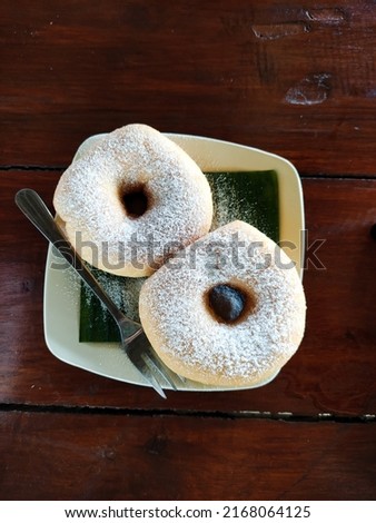donuts sprinkled with white powdered sugar on a banana leaf on a white plate