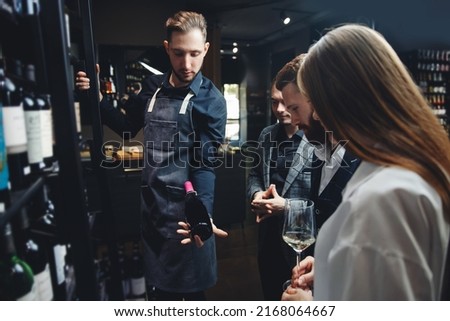 Man sommelier helps visitors to restaurant or liquor store to choose bottle of wine. Royalty-Free Stock Photo #2168064667