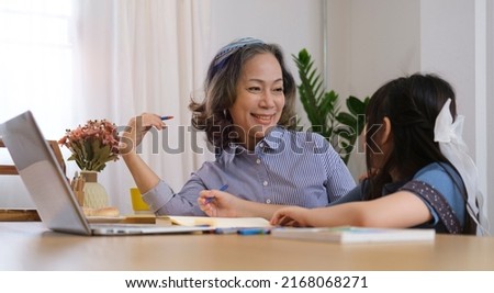 Smiling grandma and cute little girl playing game or watching cartoons on laptop, enjoying free time on weekend at home together.