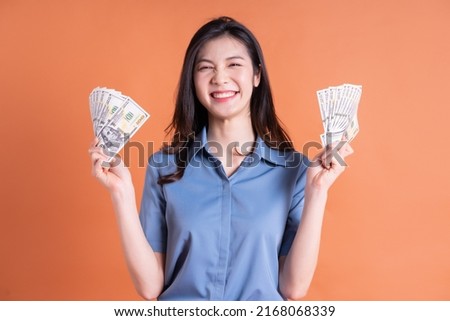 Image of young Asian woman holding money on background