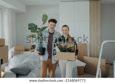 Cheerful young couple in their new apartment, carrying boxes. Conception of moving.