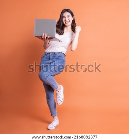 Full length image of young Asian girl using laptop on orange background