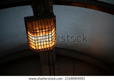 Lamp behind bars. Dim lamp light. Light system in tunnel. Square light source.
