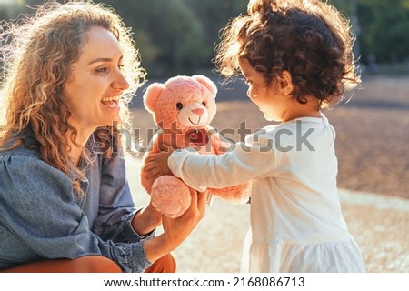 Curly single woman giving a teddy bear to her little daughter outdoors in the park - family lifestyle concept Royalty-Free Stock Photo #2168086713