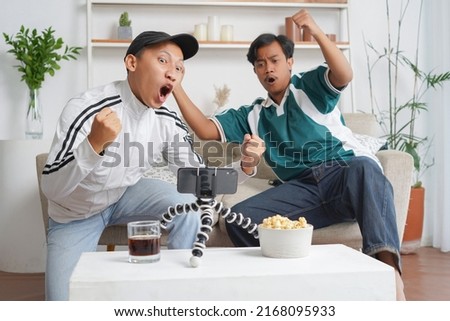 two asian men celebrate the victory of a football match via smartphone in the living room