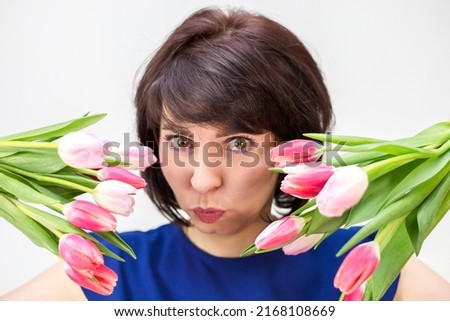 Portrait of an adult brunette covering her face with two bouquets of tulips white background.