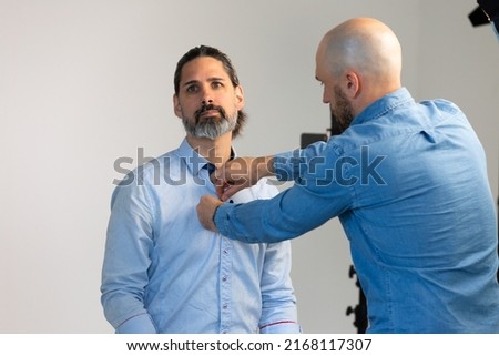 Putting Lavalier Microphone on Caucasian Male Wearing Business Attire. Video Production or Film Set Behind the Scenes. Lav Mic Clips Onto Shirt.
