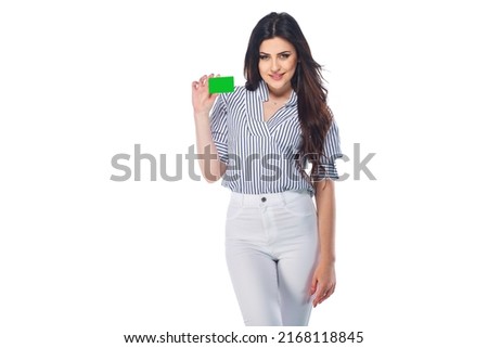 Beautiful brunnet сaucasian young girl in white pants and striped shirt holding bank or business card (saved with path) isolated on white background