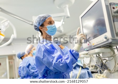 Portrait of a young female doctor in scrubs and a protective face mask preparing an anesthesia machine before an operation Royalty-Free Stock Photo #2168129057