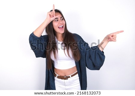 young caucasian woman wearing fashion clothes over white background showing loser sign and pointing at empty space