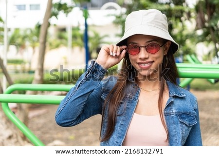 Portrait of a young, fresh young woman standing outdoors on a sunny day and looking at the camera through sunglasses.