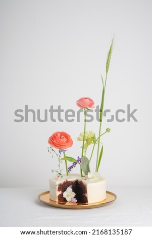 Chocolate cake with white cream decorated with fresh flowers on a light background, cut cake