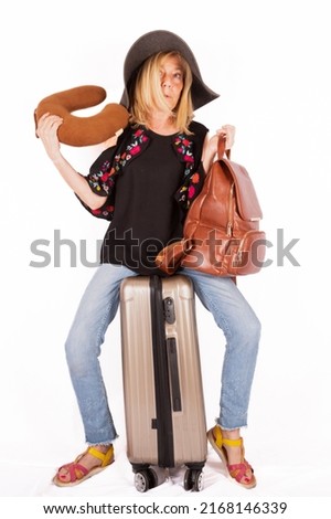Mature blonde woman, sitting on a suitcase preparing for a holiday with hat and handbag, white background