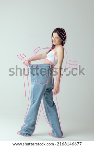 Portrait of slim woman in underwear wear posing in giant oversized jeans isolated over gray background. Lines around body before losing weight. Concept of healthy eating, dieting, weight, fitness, ad Royalty-Free Stock Photo #2168146677