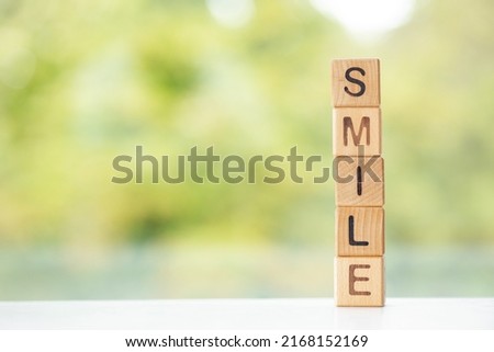 Smile word is written on wooden cubes on a green summer background Closeup of wooden elements