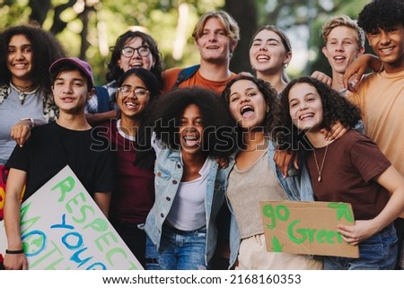 Group of multicultural teenagers smiling happily while standing together at a climate change protest. Diverse youth activists joining the global climate strike. Royalty-Free Stock Photo #2168160353