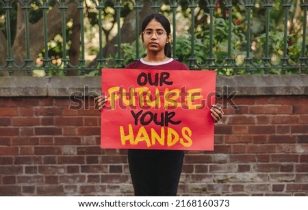 Young teenage girl looking at the camera while holding a climate change poster. Young environmental activist protesting against global warming and climate change.