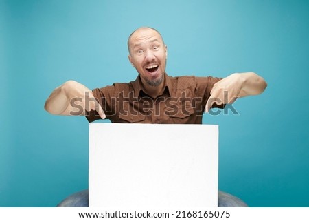  A Bald man with emotion face holding  white board in his hands to fill your text. Isolated on blue background.