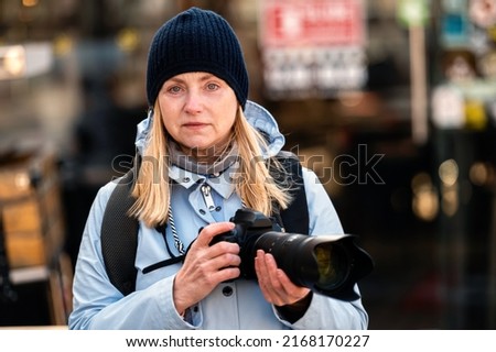 blonde middle-aged woman with a photo camera in the evening on the city streets, lifestyle concept