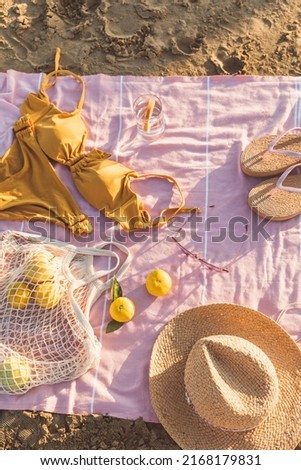 Summer beach accessories flat lay on sand background. Holiday travel, tropical concept. Straw hat, bikini, sunglasses, slippers and fruits in eco friendly mesh shopping bag. Sun shadow and sunlight.