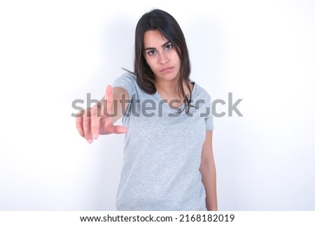 young caucasian woman wearing grey t-shirt over white background making fun of people with fingers on forehead doing loser gesture mocking and insulting.