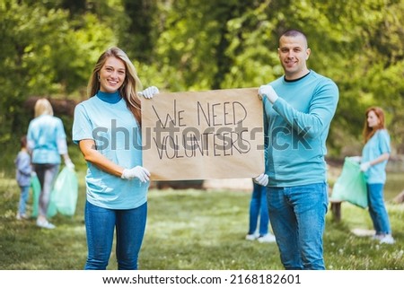 Group of young adults collaborate to organize a recycling campaign. Man and woman foreground with sign. They holds poster that she made.



