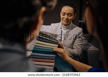 Confident clerk, saleswoman in interior design showroom showing to customers fabric samples for sofa restoration and upholstery of various colors, textures and quality. Home improvement and renovation