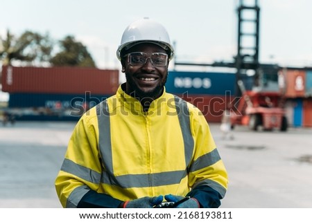 Portrait of optimistic black industrial worker smiling while looking at camera. Confident man in safety uniform at container yard.