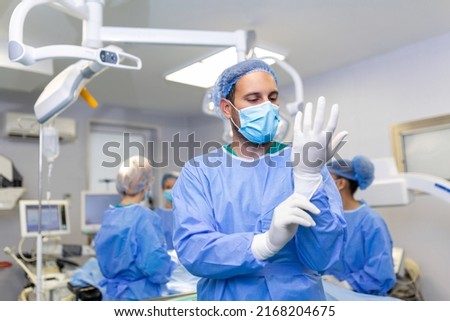 Portrait of male doctor surgeon putting on medical gloves standing in operation room. Surgeon at modern operating room