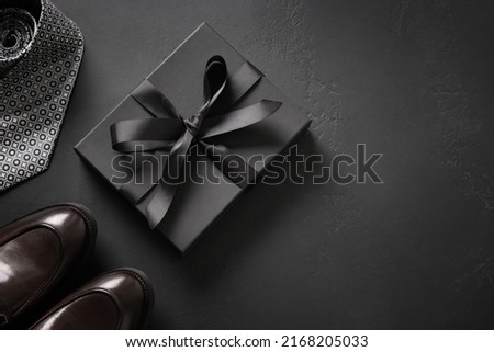 Greeting card with gift for father on black background. Set of classic mens clothes - brown shoes, tie and gift. Happy Fathers Day. Men's accessories set. Top view. Copy space. Royalty-Free Stock Photo #2168205033